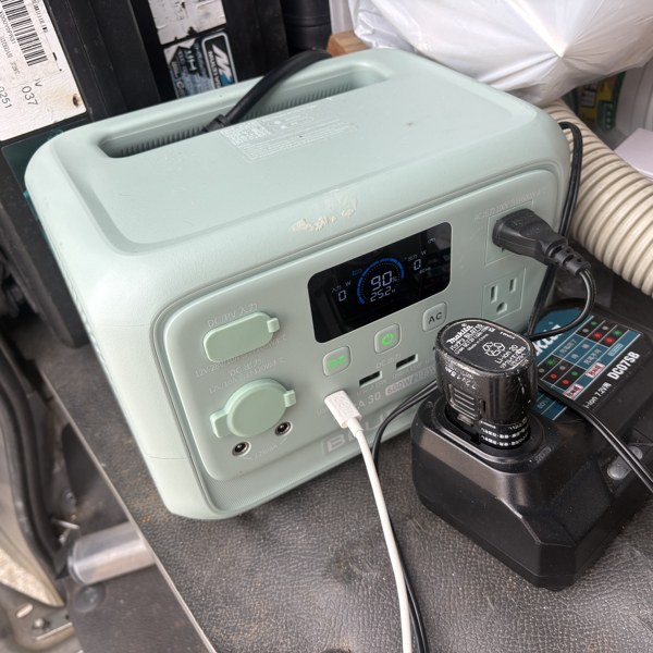 トラックの荷台でBLUETTI AORA 30 V2のACコンセントに充電器をつなぎ、電動工具のバッテリーを充電しているところ